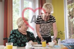 Eine Frau bringt einer alten Frau Seniorin im Rollstuhl einen Teller mit Broten
