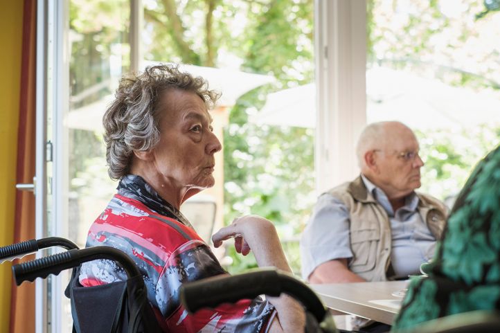 Eine alte Frau Seniorin in einem Rollstuhl sitzt neben anderen Seniorinnern und Senioren