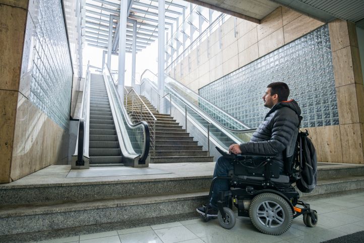 Behinderter Mensch im Rollstuhl vor einer Rolltreppe