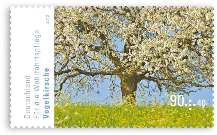 Auf der Briefmarke ist eine grüne Wiese und ein großer blühender Baum 