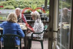 Zwei Seniorinnen und ein Senior sitzen auf einem Balkon und spielen Karten