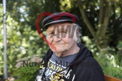 Ein alter Mann Senior sitzt auf einer Parkbank und blickt in die Kamera