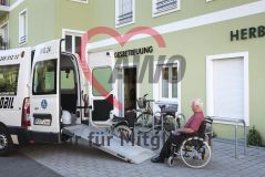 Ein alter Mann Senior im Rollstuhl sthet vor einer Rampe eines Transporters vor einer AWO Tagesbetreuung