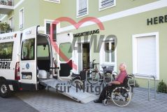 Ein alter Mann Senior im Rollstuhl sthet vor einer Rampe eines Transporters vor einer AWO Tagesbetreuung