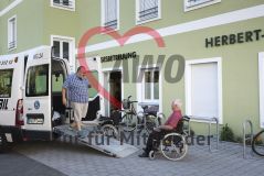 Ein Mann kommt aus einem Transporter zu einem alten Mann Senior im Rollstuhl