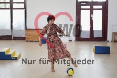 Eine alte Frau Seniorin spielt Fußball in einer Turnhalle