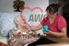 Eine Frau hilft einer alten Frau Seniorin im Bett beim Trinken