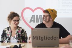 Eine junge Frau und junger Mann mit einem Laptop Notebook Rechner sitzen nebeneinander und lachen