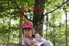 Mädchen mit AWO-Käppi im Wald, auf einem Baumstamm kletternd